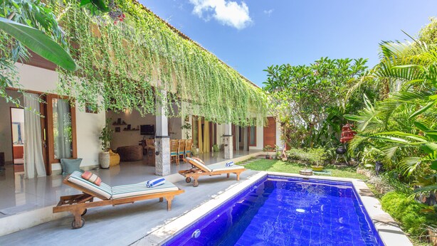 A poolside area with lounge chairs, a swimming pool, and lush greenery. - MasBro ART Villas (Seminyak)