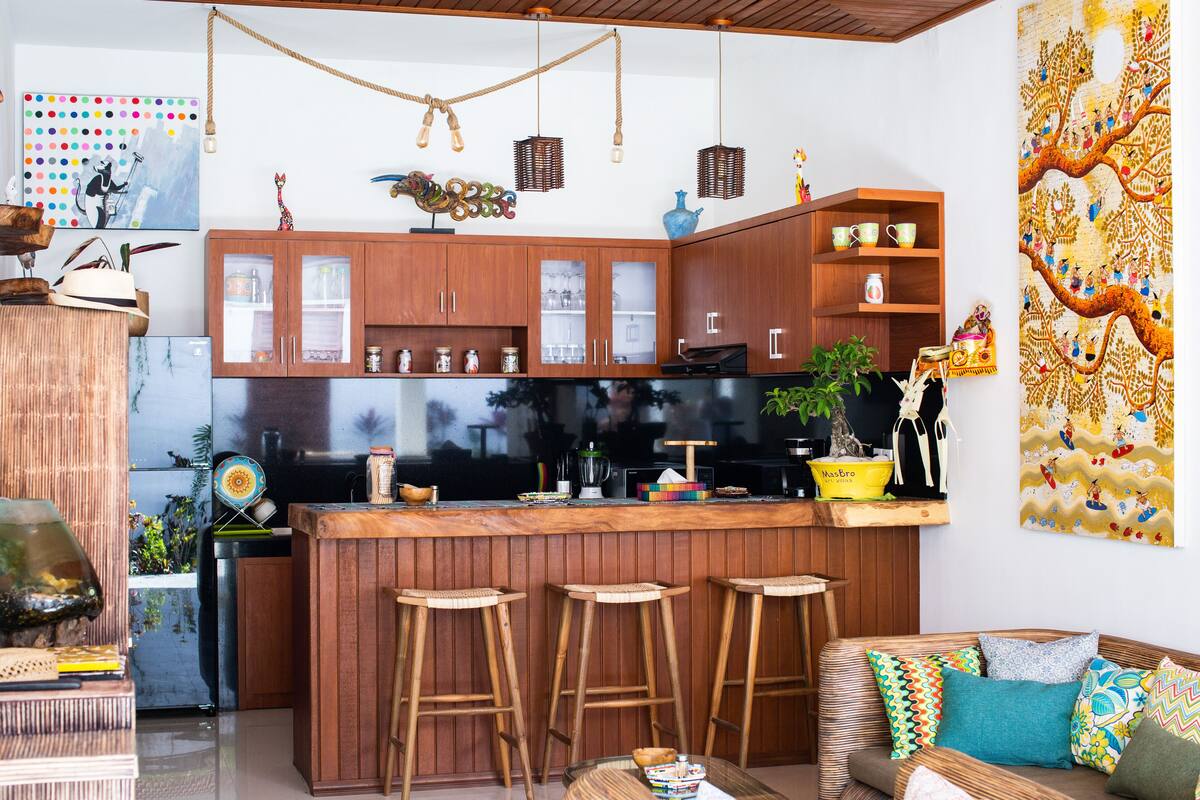 A modern kitchen with wooden cabinets, a central island with stools, and a large decorative wall piece.