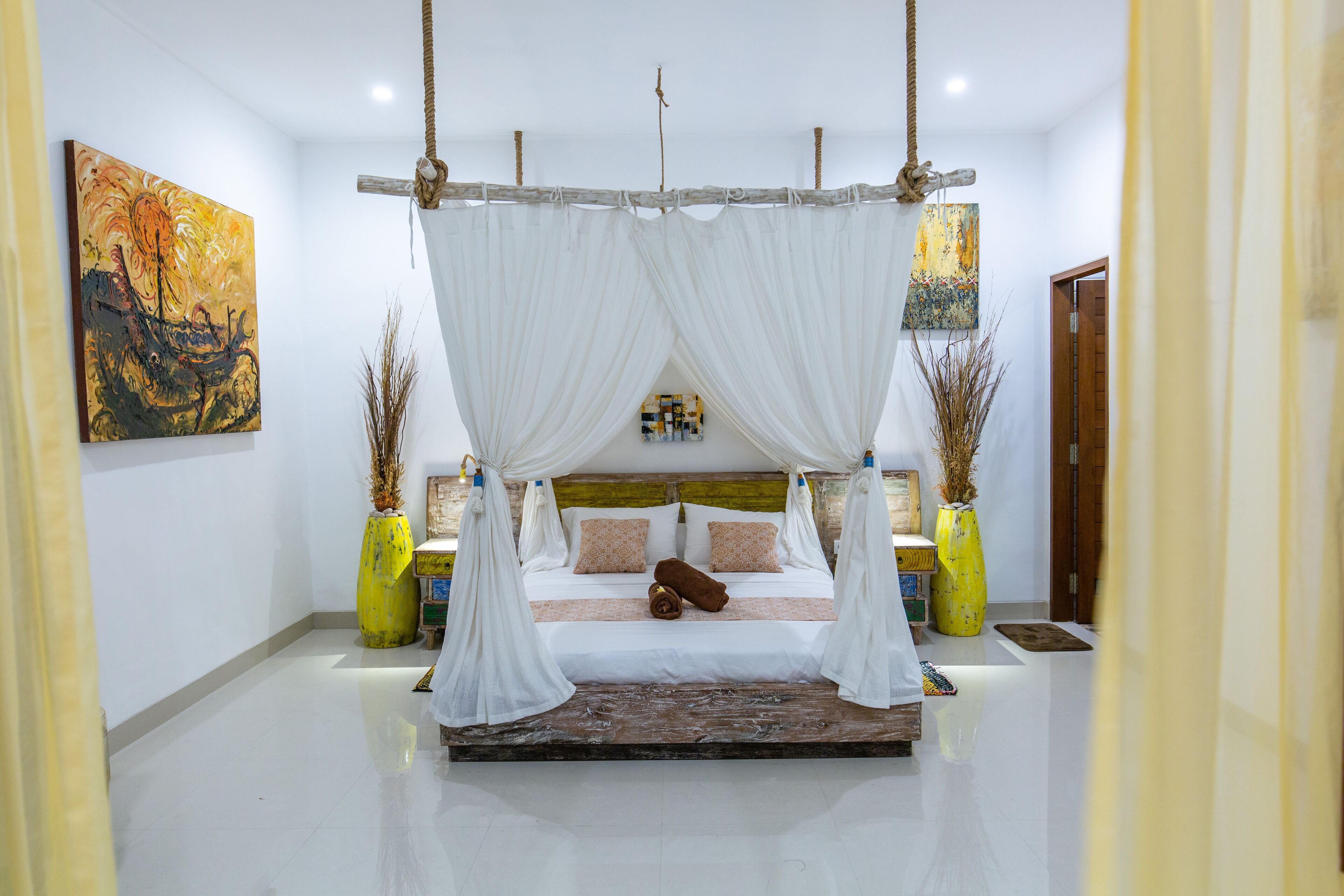 A spacious bedroom with a large bed, white drapes, and two yellow vases.