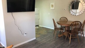 A dining area with a wooden table and chairs, a mounted TV, and a decorative mirror on the wall.