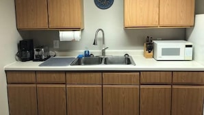 A kitchen with wooden cabinets, a stainless steel sink, a coffee maker, a microwave, and a blue decorative plate on the wall.