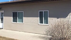 A single-story building with a beige siding exterior, two windows with white frames, and a small porch area.