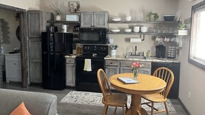 A compact kitchen with a dining area, featuring a black refrigerator, a microwave, a stove, and wooden chairs around a round table. - Secluded Peaceful Chalet 1 Bdrm King Suite AC, Private Laundry Room (Bigfork)