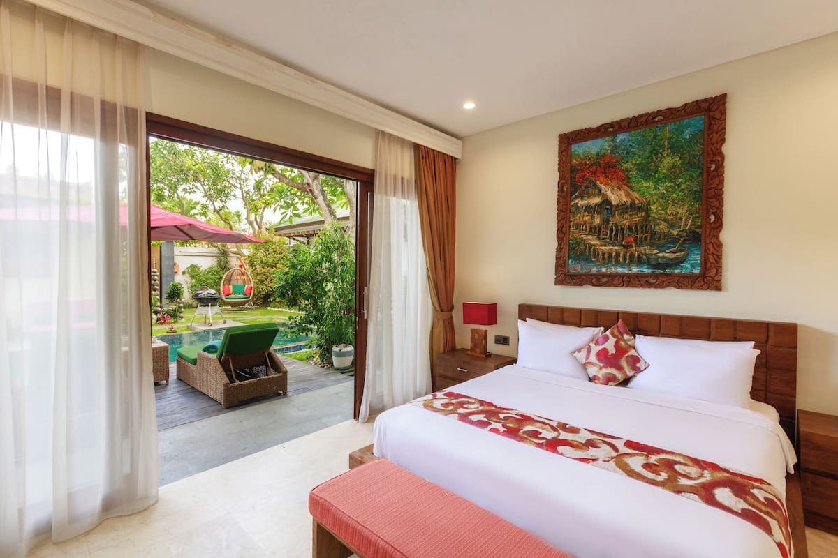 Une chambre d’hôtel avec un grand lit, un tableau au mur et une vue sur un jardin et une piscine.