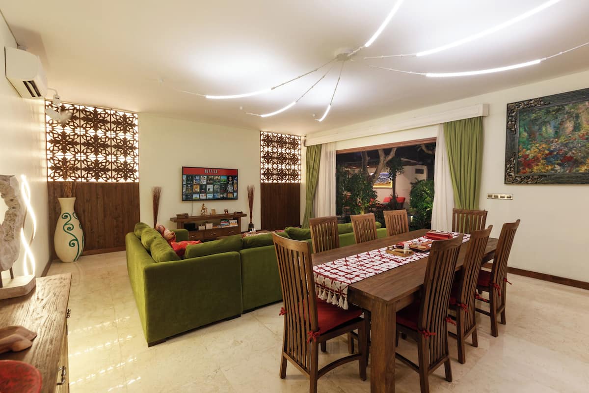Un coin repas avec une table et des chaises en bois, un canapé vert, des panneaux décoratifs et un tableau au mur.
