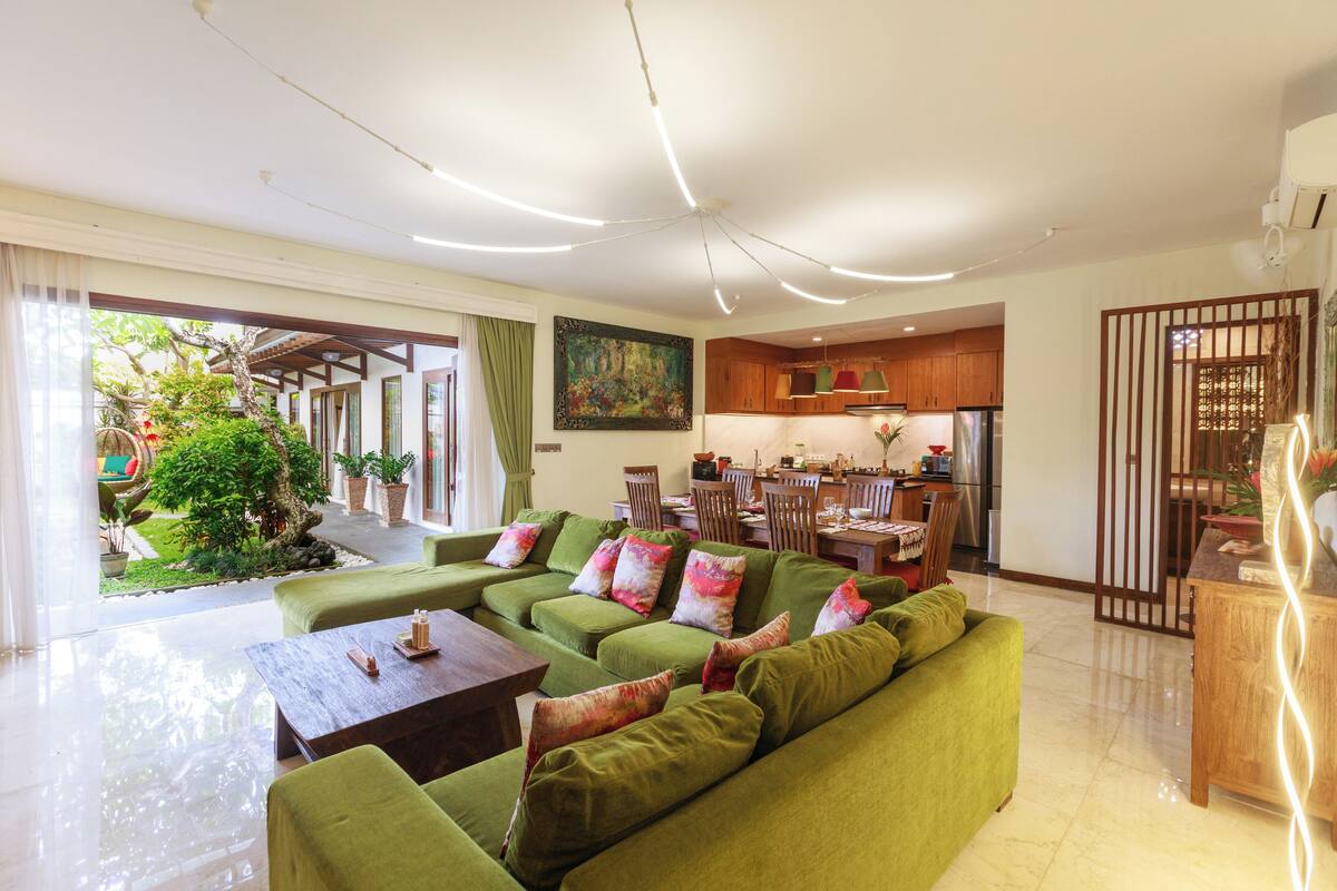 Un vaste espace de vie comprenant un canapé vert, une table basse en bois et un coin repas avec des chaises et une table en bois.