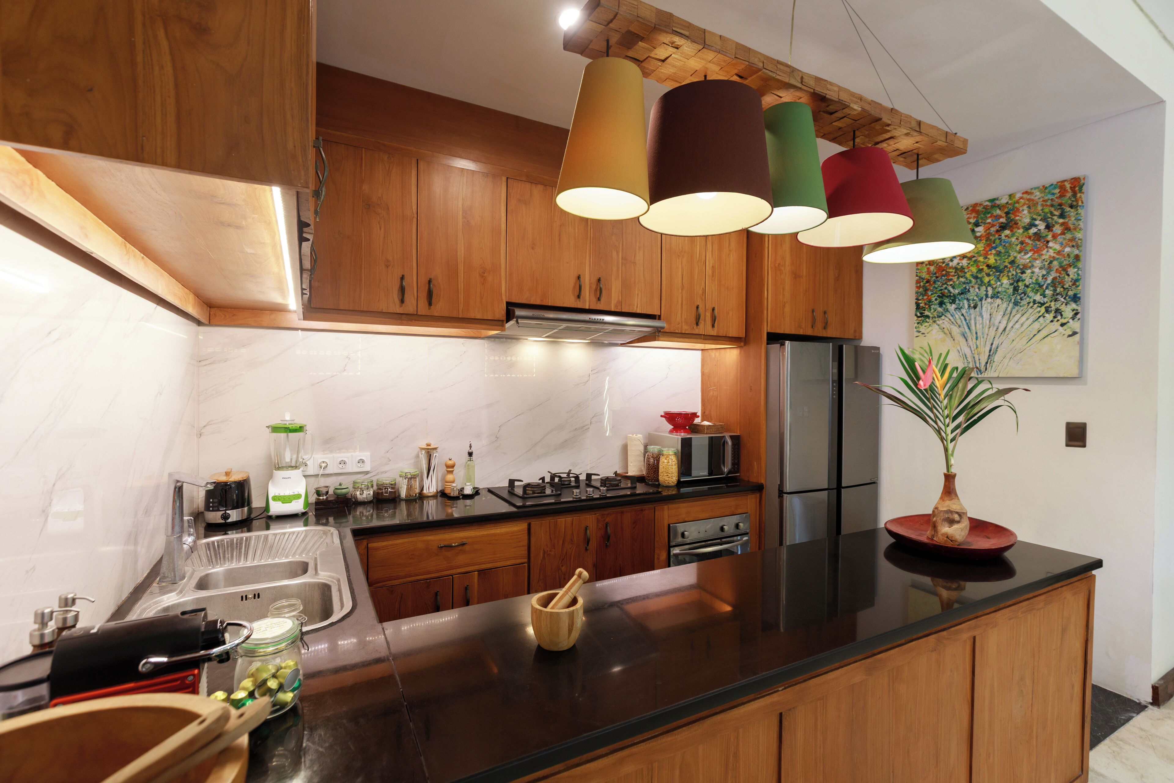 Une cuisine moderne avec des meubles en bois, un plan de travail noir et des suspensions colorées.