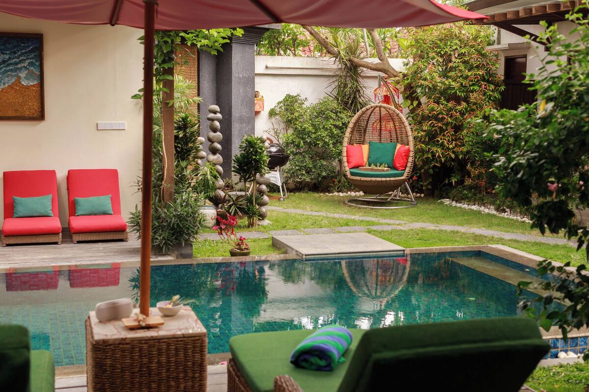 Un espace aménagé au bord de la piscine, avec des chaises longues, un fauteuil suspendu et un petit jardin.