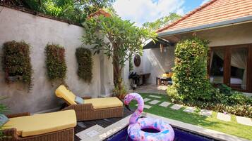 Relax in a serene garden setting with a pool, wicker lounge chairs, and lush greenery.