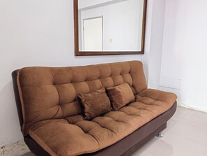 A brown sofa with a cushion, positioned against a white wall with a framed mirror above it. - Mailbox Arsakha Lobi B Cibubur Village (Depok)
