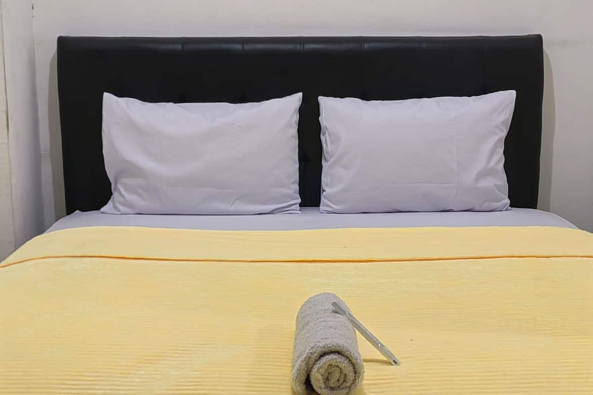 A bed with a black headboard, two white pillows, and a yellow bedspread.