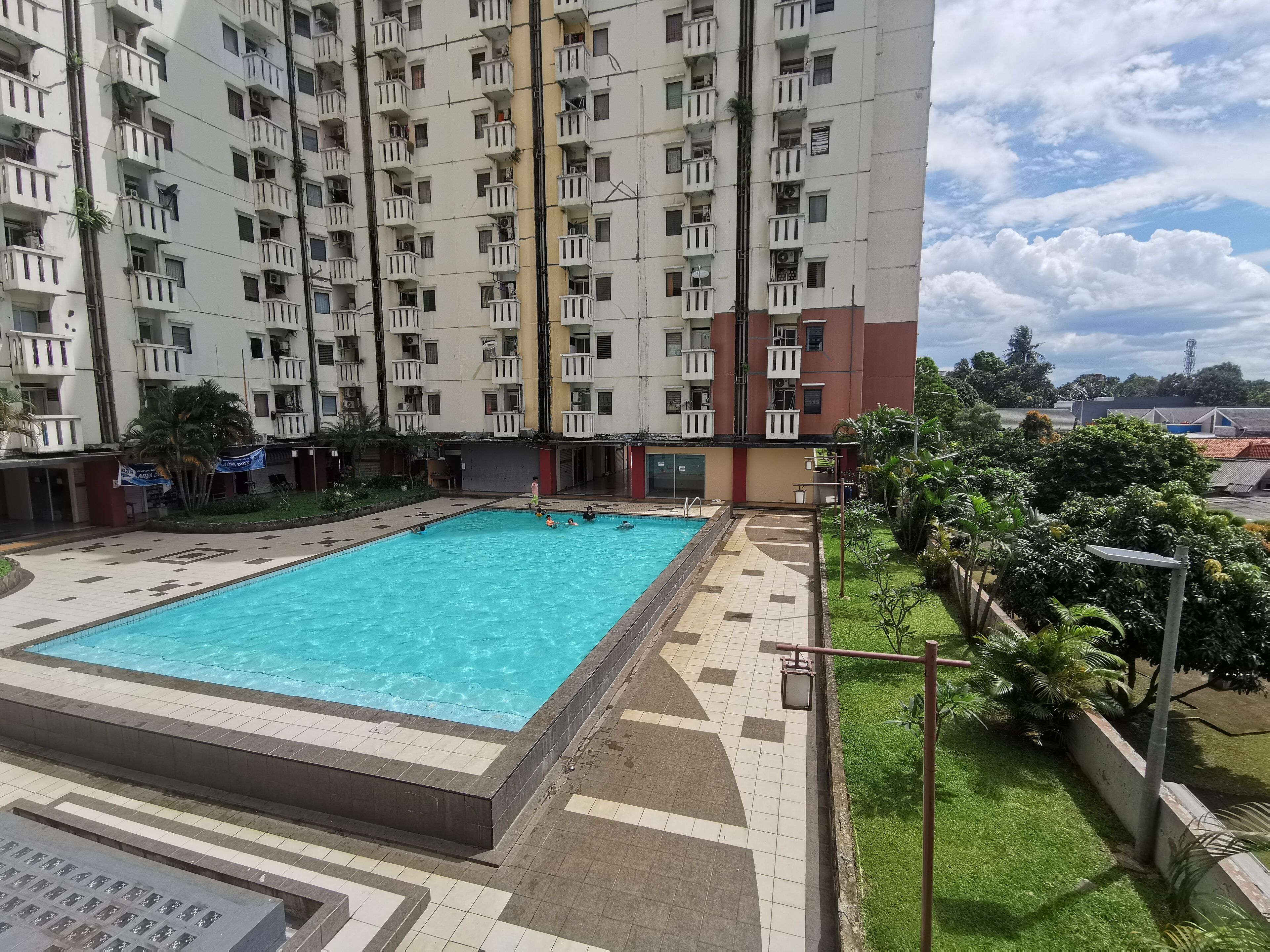 Una piscina rodeada de un solárium con baldosas, con un rascacielos al fondo.