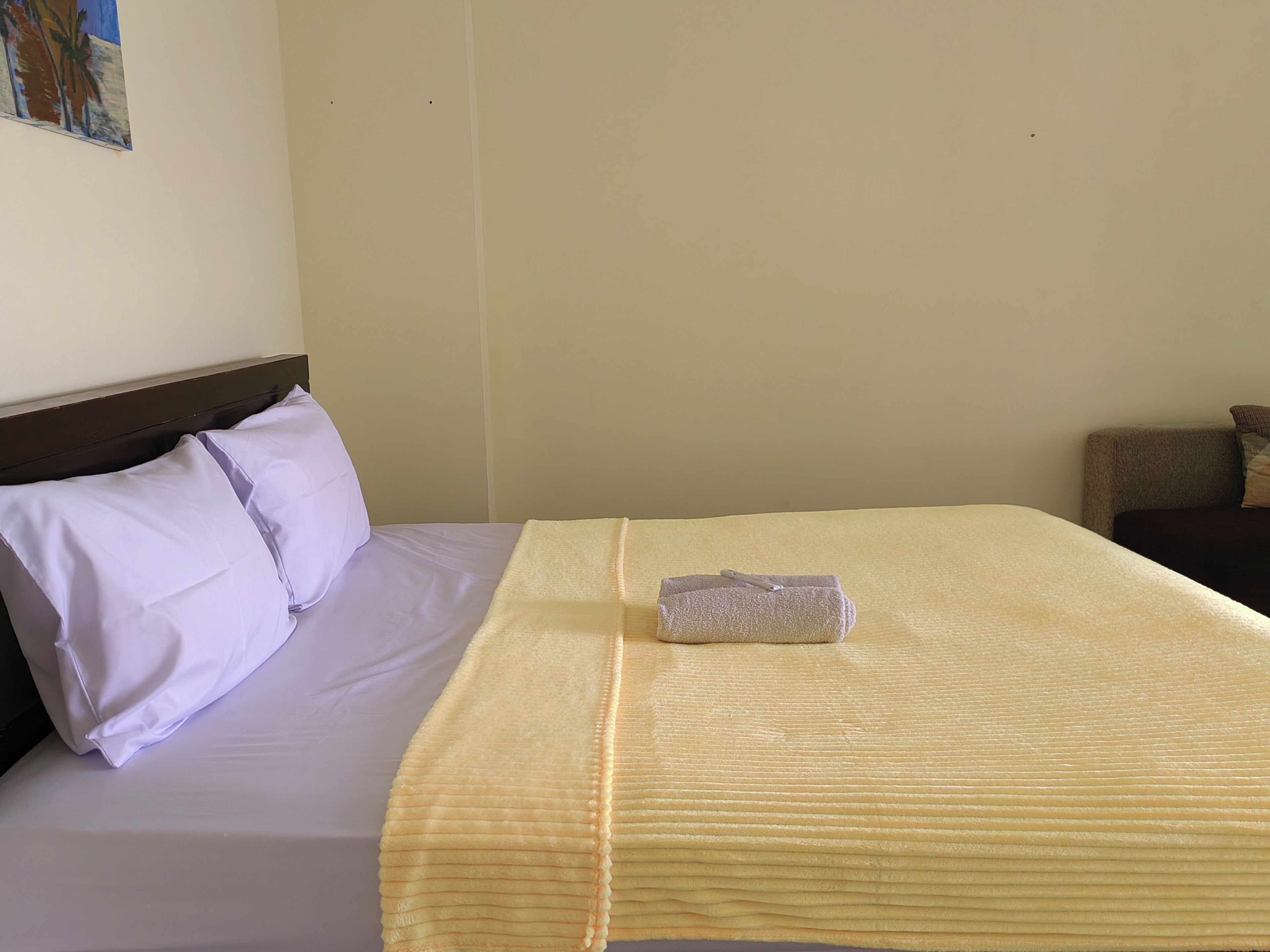 Un letto rifatto con una coperta bianca e gialla, un asciugamano piegato e due cuscini.