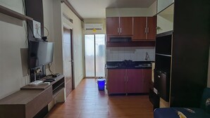 A compact living space with a kitchenette, a flat-screen TV mounted on the wall, and a sliding door leading to an outdoor area.