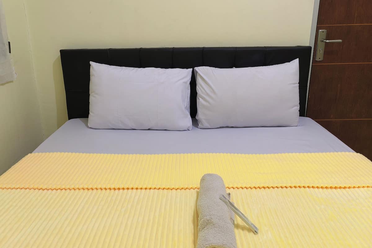 A bed with a black headboard, two white pillows, and a yellow striped bedspread.