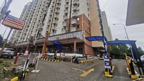 A high-rise building with multiple balconies, a sign for Alfamart, and a gated entrance with directional arrows.