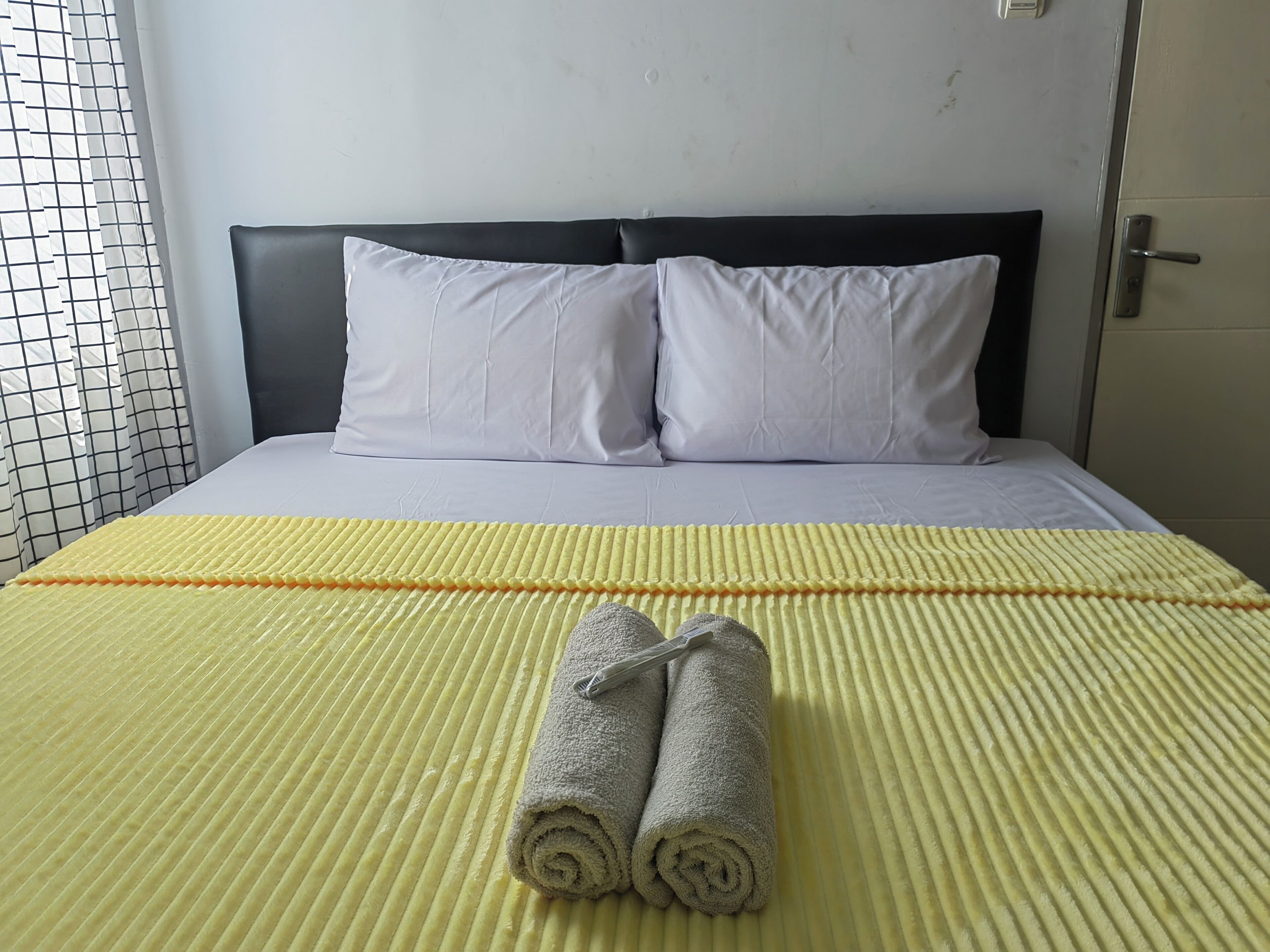 Una cama bien hecha con almohadas blancas y una colcha amarilla a rayas.