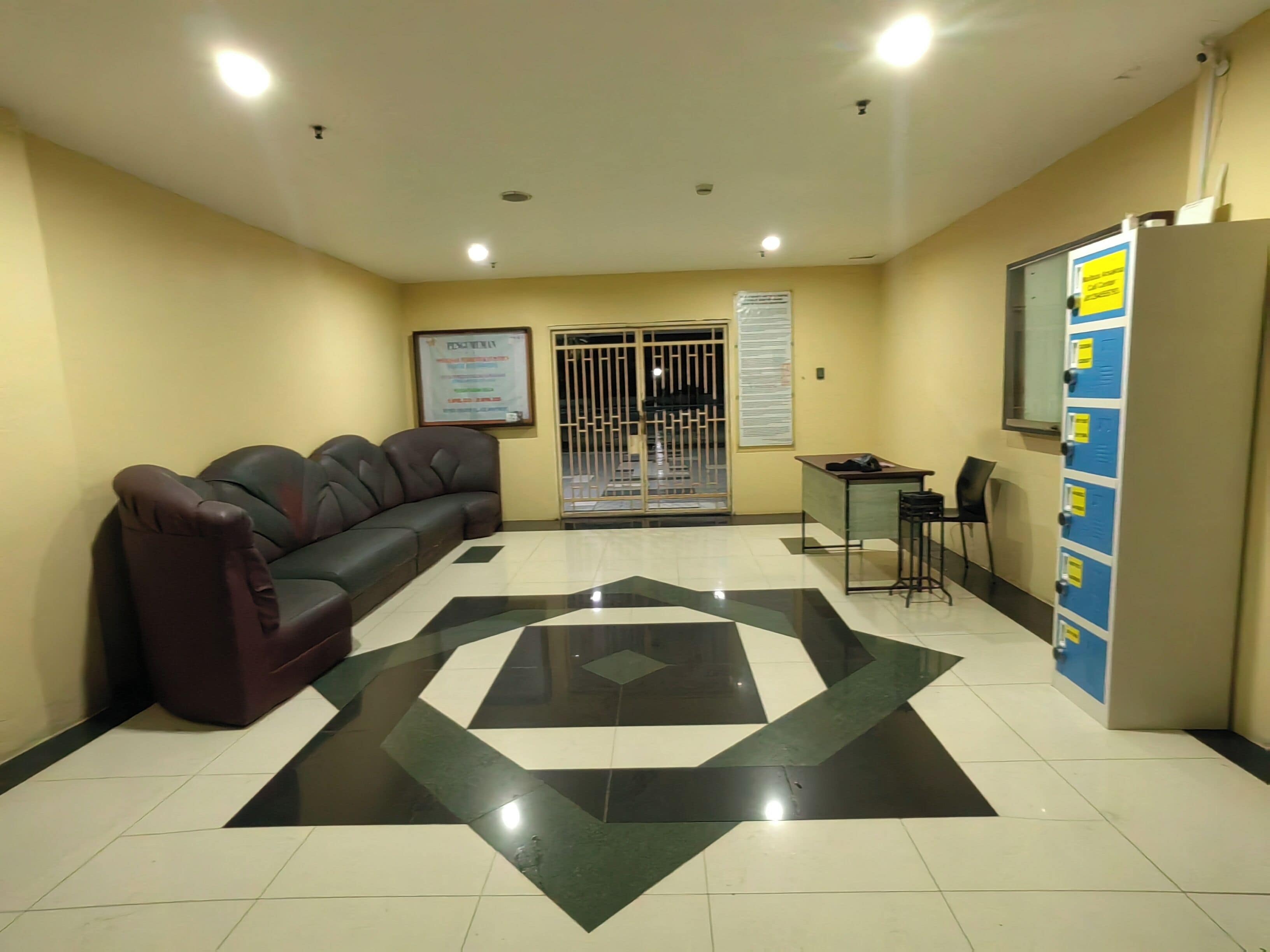 A reception area with a black and white tiled floor, a brown leather sofa, a small table with a chair, and a blue and white locker unit.