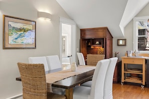 Un coin repas comprenant une table en bois foncé, des chaises à revêtement blanc, une chaise en osier et un petit meuble en bois doté d’étagères.