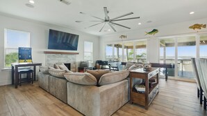 A spacious living room with a large sectional sofa, a ceiling fan, and a view of the ocean through large windows.