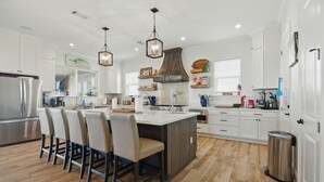 A modern kitchen with white cabinetry, a central island with bar stools, a stainless steel refrigerator, and pendant lighting.