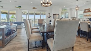 A spacious dining area with a large wooden table and upholstered chairs, a chandelier, and nautical-themed decor.