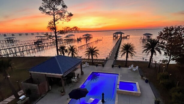 A pool area with lounge chairs and umbrellas, overlooking a waterfront with docks and palm trees.