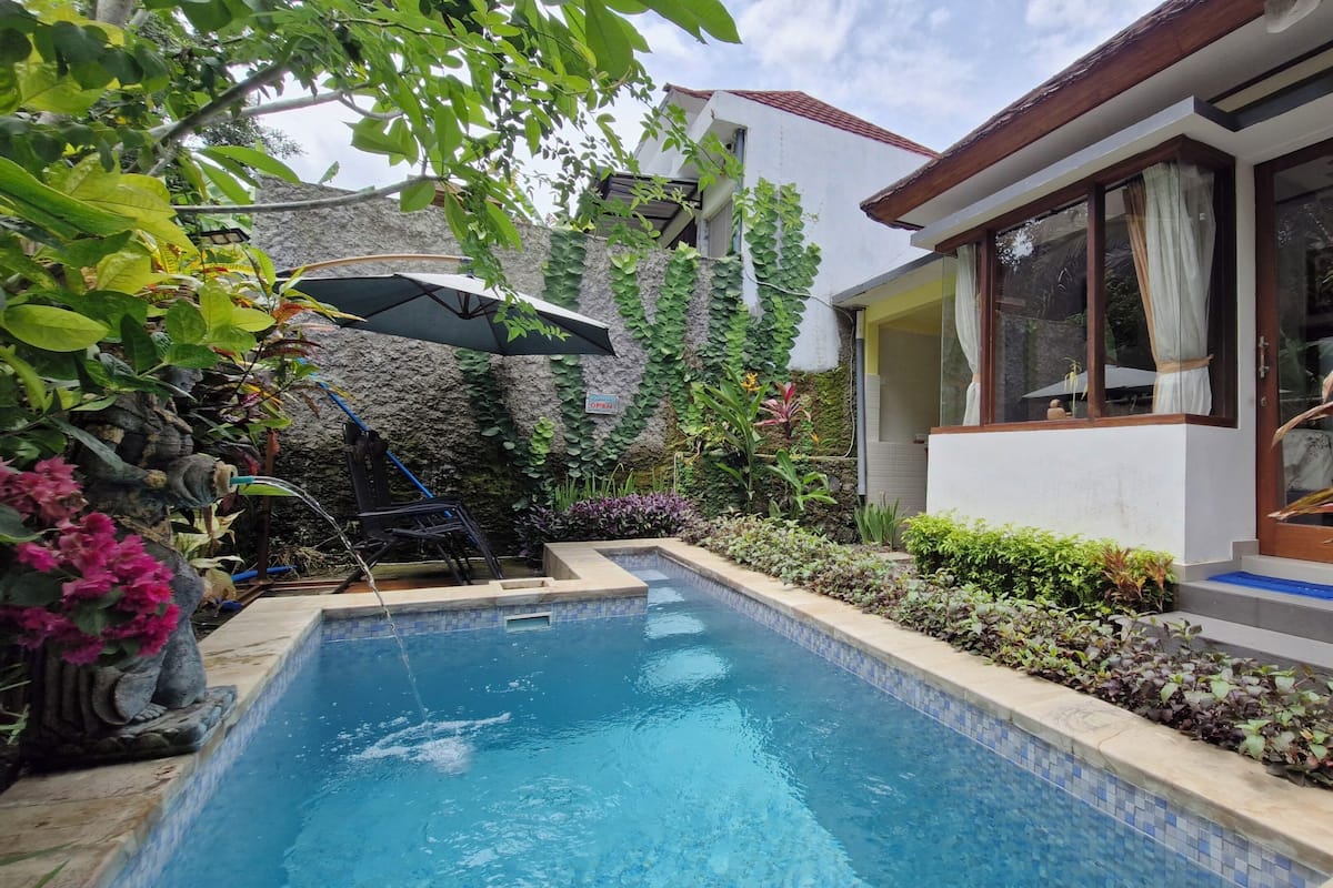 Piscina rodeada por vegetação exuberante e um edifício branco com grandes janelas.
