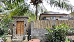 Un giardino tropicale con un ingresso in pietra, una porta in legno e un tavolo rosso.