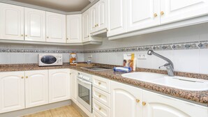 A kitchen with white cabinets, a granite countertop, a microwave, a stove, and a sink.