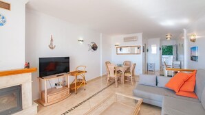 A living room with a TV, wooden furniture, a fireplace, and a dining area with chairs and a table.
