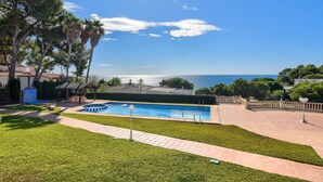 A swimming pool with a view of the sea, surrounded by well-maintained grass and trees.