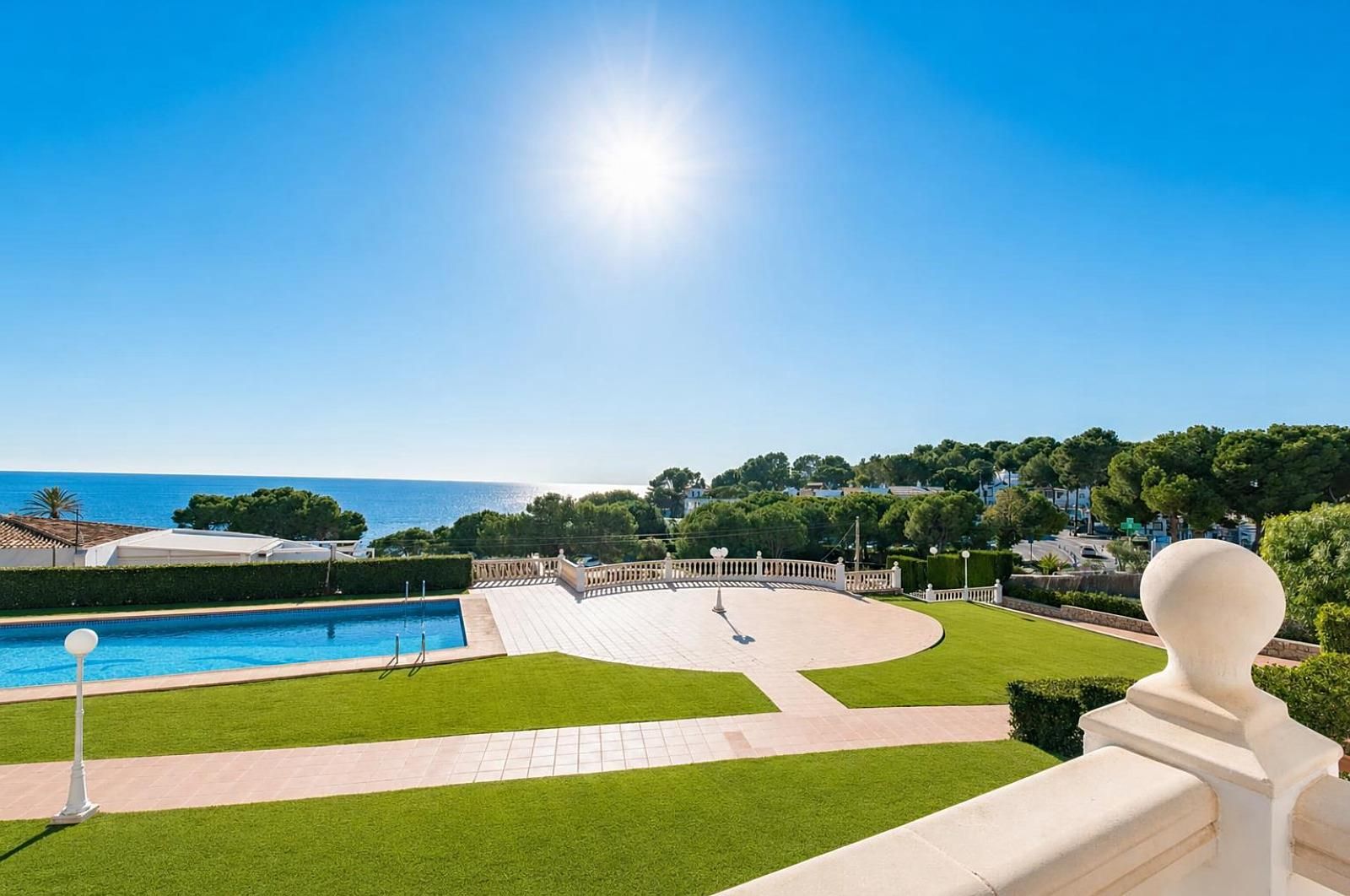 Un espace piscine offrant une vue dégagée sur la mer, une pelouse bien entretenue et une balustrade blanche.