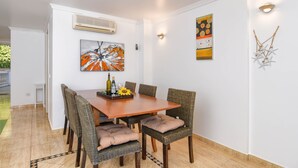 A dining area with a wooden table, wicker chairs with cushions, and wall art. - Poolbeach VI 4 pax - Moraira, Costa Blanca (Moraira)