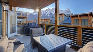 Una terraza de madera con una mesa, sillas, una parrilla y vistas a las montañas.