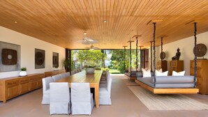 A spacious room with a long wooden dining table, cushioned seating, a hanging swing, and a ceiling fan. - Baan Kilee (Koh Samui)