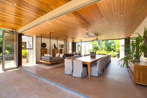 A spacious indoor area with a wooden ceiling, a large dining table with chairs, a sofa, and a ceiling fan.