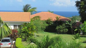 A coastal property with a tiled roof, lush greenery, and a view of the ocean.