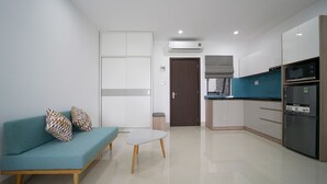 A modern living room with a sofa, a coffee table, and a kitchen area with cabinets and appliances. - Sunny Studio with balcony ★ Steps to Dragon Bridge (Đà Nẵng)