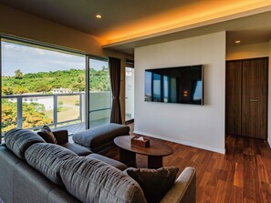A modern living room with a large window, a sofa, a coffee table, and a flat-screen TV mounted on the wall. - Private Condo Chatan Jagaru by Coldio Premium (Chatan)