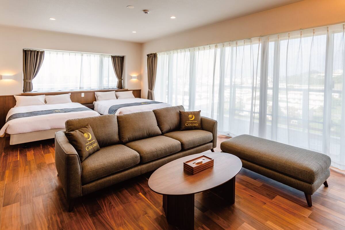 A hotel room with two beds, a sofa, an ottoman, and a round coffee table.