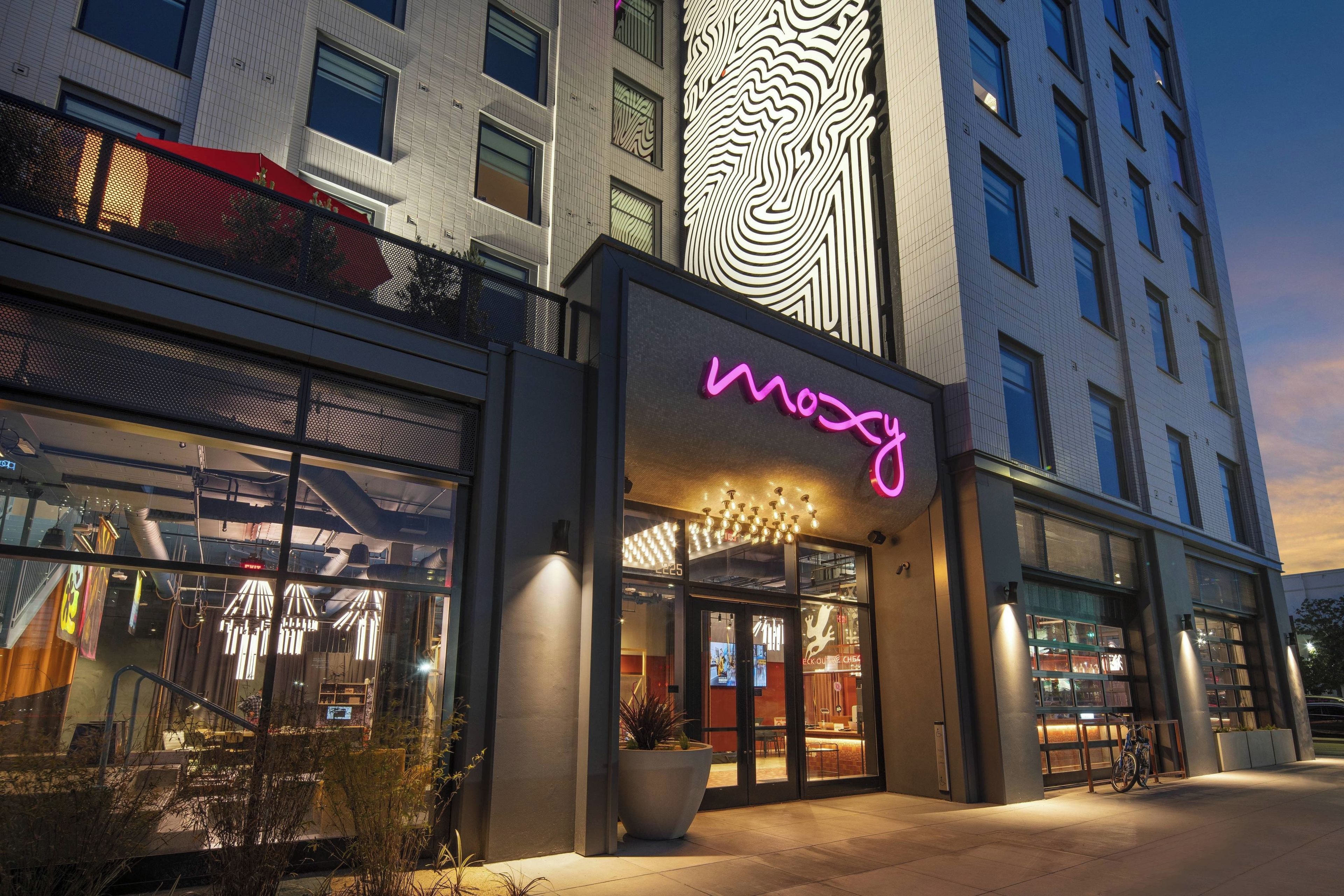 A modern building with a neon sign reading 'mooy' and a large window displaying interior lighting.