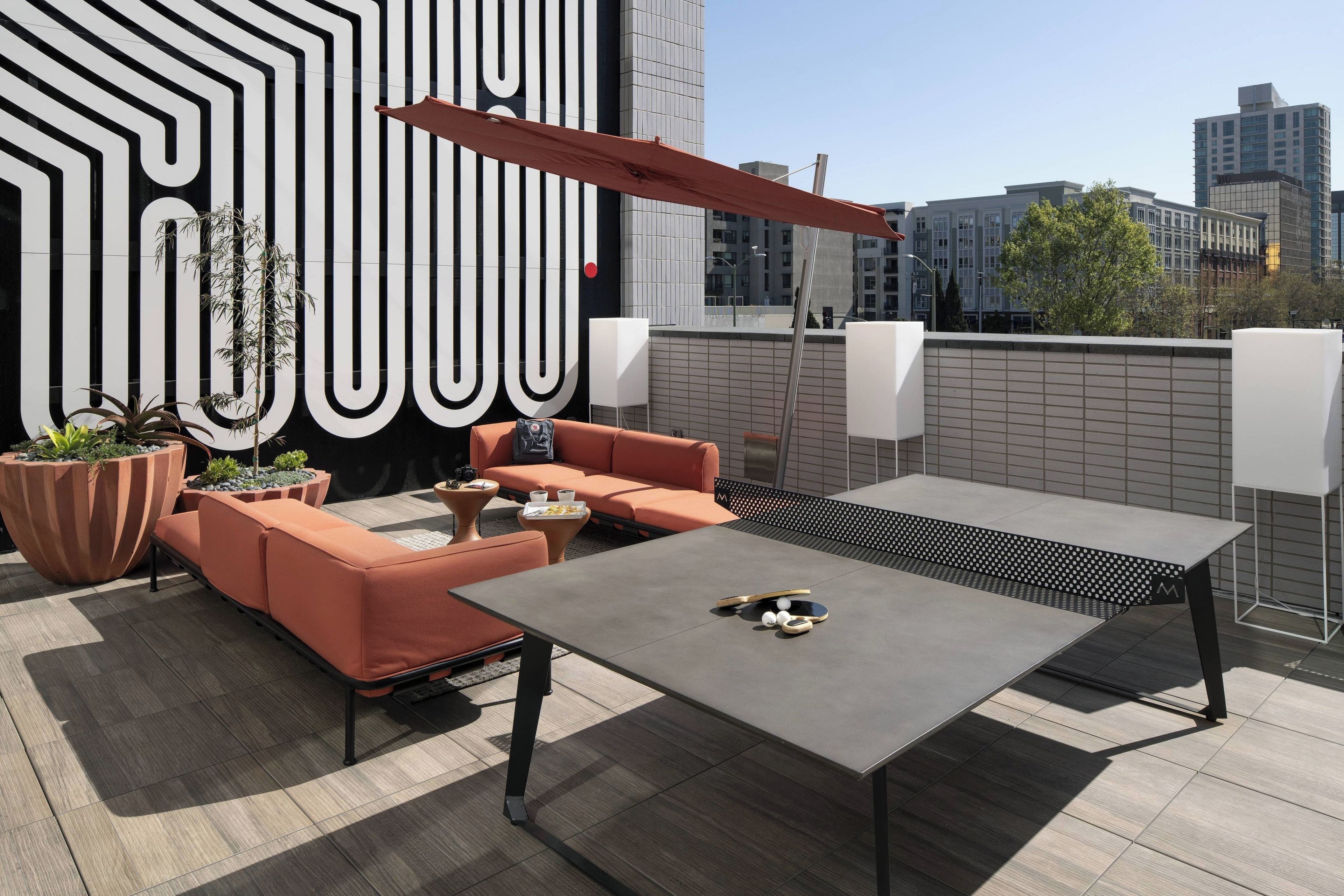 An outdoor seating area with a table and chairs, a large planter, and a wall with a geometric pattern.