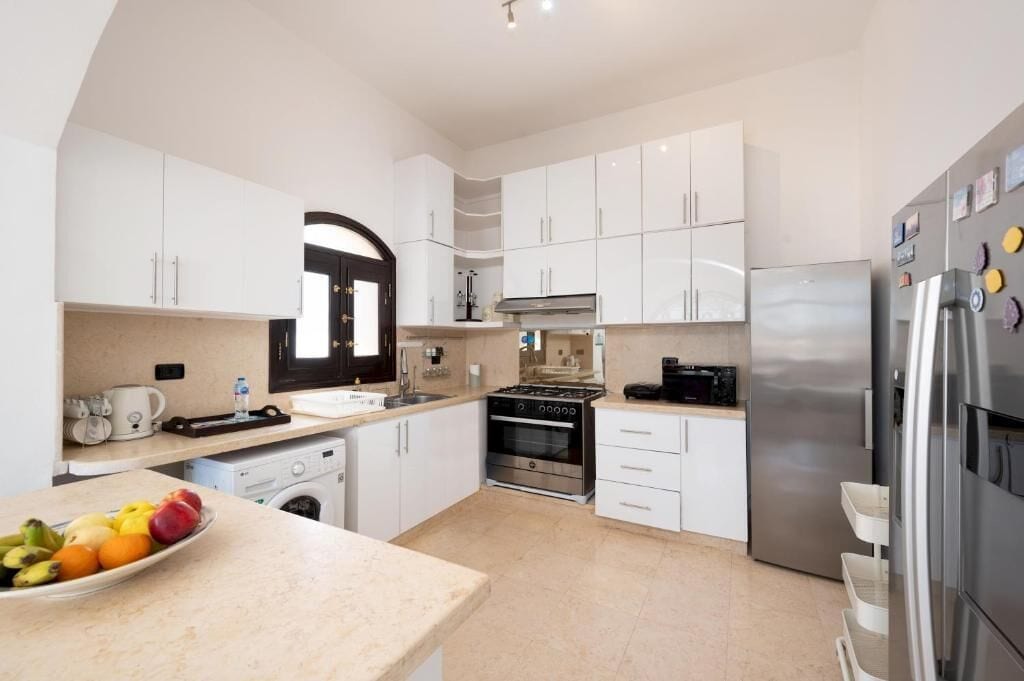 A modern kitchen with white cabinets, stainless steel appliances, and a bowl of fruit on the counter.