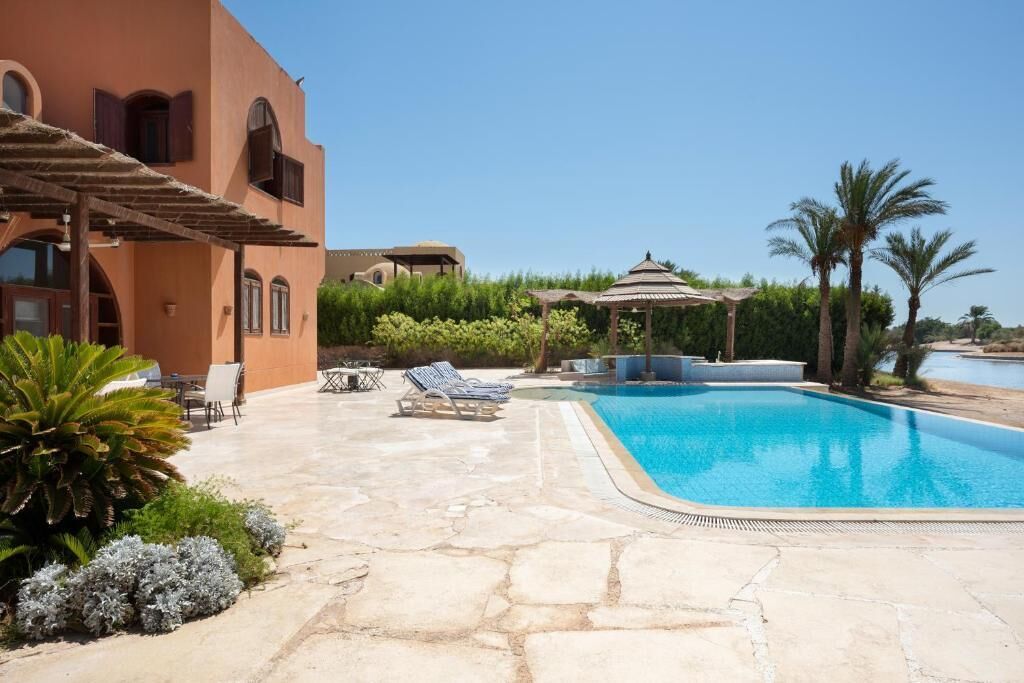 A swimming pool with lounge chairs, a pergola, and a gazebo in a landscaped outdoor area.