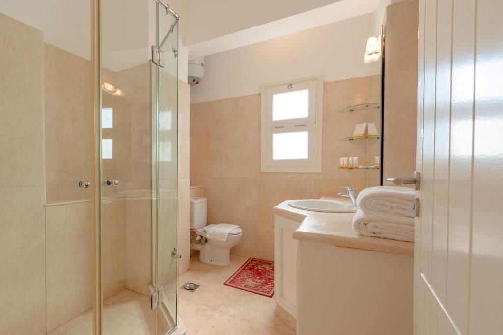 A modern bathroom with a glass shower enclosure, a toilet, a sink with a mirror, and a small window.