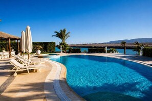 A clear blue swimming pool with lounge chairs and umbrellas, surrounded by greenery and a view of the sea. - VESTA - El Gouna Residence (El Gouna)