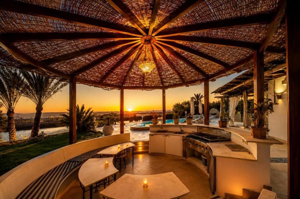 Eine Außenpatio mit einer runden Sitzgruppe, einem eingebauten Grill und Blick auf den Sonnenuntergang über dem Wasser.