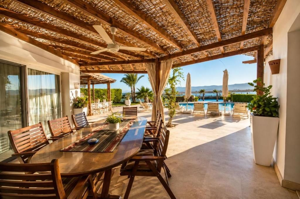 Un área de comedor al aire libre con pérgola, piscina y sillas junto a la piscina.
