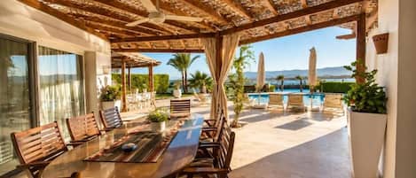 Un área de comedor al aire libre con pérgola, piscina y sillas junto a la piscina.